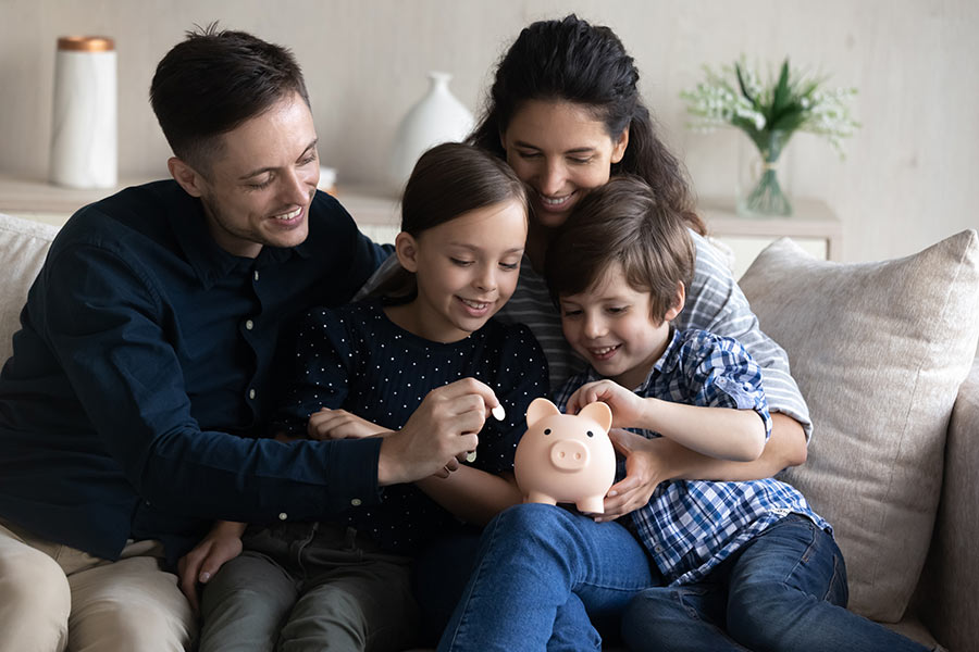 Happy family teaching kids about saving money with a piggy bank while sitting together on a couch at home